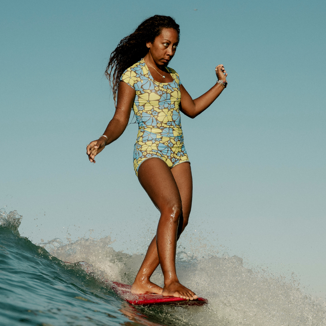 Woman in floral swimsuit surfing on a wave.